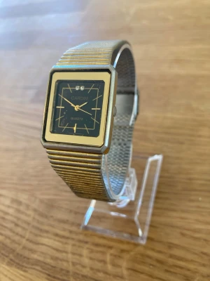 Gardini Gold Square Quartz Armbandsur - Ett Gardini Quartz armbandsur med en fyrkantig boett i guldton och en svart urtavla. Urtavlan har minimalistiska markeringar och två dekorativa stenar vid klockan 12. Klockan har ett integrerat länkarmband i guldton och silverfärgat stål med ett viklås. Klockan är i gott skick med mindre tecken på användning. Behöver bara nytt batteri.  Mitt pris: 189 SEK  Skickas snabbt och spårbart. Skriv vid frågor och se gärna mina andra annonser!