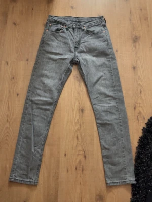 Grå Levi's jeans med raka ben - Snygga grå jeans från Levi's med klassisk femficksdesign och raka ben. Jeansen har en stilren look med diskreta sömmar och läderpatch bak i midjan. Perfekta för dig som gillar en enkel och tidlös stil. Stl 31/32
