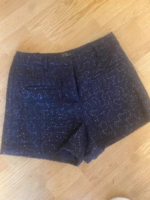 Mörkblå glittriga shorts från Ais U - Snygga mörkblå shorts från Ais U med glittriga paljetter över hela tyget. Klassisk passform med fickdetaljer fram och bälteshällor. Perfekta för att sticka ut och ge outfiten extra edge.