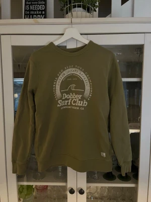 Olivgrön sweatshirt Dobber Surf Club - Säljer denna tröja från dobber. Tröjan är i storlek M men passar även S bra. Den är i fint skick med ett schysst märke på bröstet. Hör av dig vid intresse eller minsta fråga.