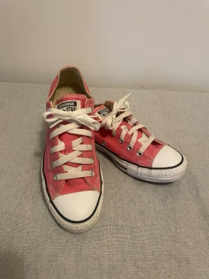 Rosa Converse All Star låga sneakers - Säljer ett par klassiska Converse All Star sneakers i rosa canvas med vita gummisulor och tåhätta. Skorna har vita snören och silverfärgade öljetter. Perfekta för dig som gillar en färgglad och tidlös stil.