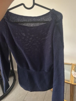 Mörkblå stickad tröja med struktur - Mörkblå stickad tröja med lång ärm och bred ribbad nederkant. Tröjan har en lös passform och är stickad i ett tunt, något genomskinligt material. Perfekt för lager-på-lager och chill stil.