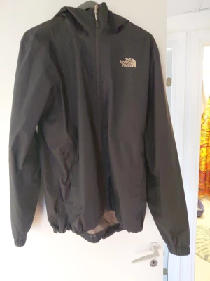 Svart vindjacka från The North Face - Inklpt hösten 2025 Svart vindjacka från The North Face med huva och dragkedja framtill. Jackan har två sidofickor och elastiska muddar vid ärmslut och nederkant. Perfekt för blåsiga dagar och enkel att matcha med olika outfits. 