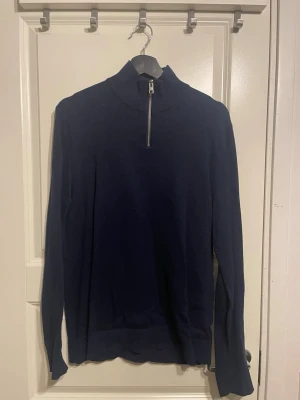 Mörkblå stickad half zip tröja - Mörkblå stickad tröja med hög krage och dragkedja framtill. Tröjan har långa ärmar och ribbade muddar vid ärmslut och nederkant. Perfekt för lager på lager och enkel att styla till olika outfits.