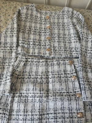 Rutig kofta och kjol set med guldknappar - Söt kofta och kjol i vit och svart rutigt tyg med dekorativa guldknappar framtill. Koftan har lång ärm och är tillverkad i ett strukturerat material. Perfekt för dig som gillar klassiska och trendiga pagg. Använd bara ett par gånger. I jätte bra skick 