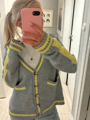  Zara kofta  - Säljer en mysig grå kofta med gula ränder och knappar framtill. Koftan har två fickor och ribbade muddar. Perfekt att slänga på sig över en t-shirt för en chill look.