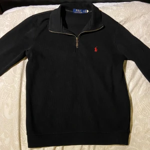 Svart half zip tröja från Polo Ralph Lauren - Svart långärmad tröja från Polo Ralph Lauren med klassisk röd logga broderad på bröstet. Tröjan har en hög krage med half zip-dragkedja och är tillverkad i mjuk bomull. Perfekt för lager-på-lager och snygg till jeans. 