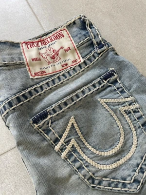 True religion Ricky super trelaxed straight unisex denim jeans Rickie loose y2k vintage premium - Säljer ett par ljusblå jeans från True Religion med ikoniska kontrastsömmar och stor broderad logga på bakfickan. Klassisk femficksmodell i denim med snygg tvätt och detaljerade sömmar. Perfekta för dig som vill sticka ut med en streetig Mått 📏 Totallängd: 107cm Midjelängd: 40cm  Innersömmlängd: 81cm Lårviddlängd: 25cm Skador 🔧: Inga  Storlek 🧍: 31  Passform: Ricky (Relaxed Straight)  Jag kan förhandla mig till lägre pris.🙋💵 Om du har några frågor, vänligen skriv till mig 🤗