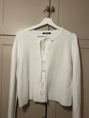 Vit stickad tröja med knyt från Gina Tricot - Säljer en vit stickad tröja från Gina Tricot med långa ärmar och tre dekorativa knyt framtill. Tröjan har en rak passform och rund halsringning. Perfekt för dig som gillar en enkel men trendig look.