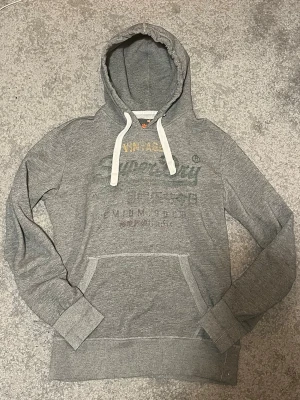 Grå hoodie från Superdry (S/M) - Säljer nu denna Grå Superdry hoodie. Är i str M men sitter mer som en S. Den är i mycket bra skick och har ett snyggt fadeat tryck på framsidan. Hör av dig vid frågor! :)