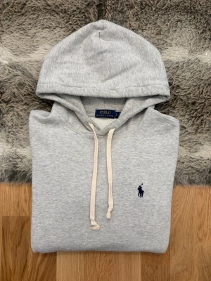 Ljusgrå Polo Ralph Lauren Hoodie - Hej! 👋 Säljer en riktigt fin ljusgrå Polo Ralph Lauren hoodie i storlek S. Den har den stilrena mörkblå pony-loggan broderad på bröstet 🐎 Tröjan är i ett gott skick. Finns en mycket liten nästintill osynlig fläck på ena ärmslutet (se sista bilden för närbild). Det är inget som drar ner helhetsintrycket när den bärs! ✨ Den är 100% äkta med tvättlappar kvar. Ett klassiskt och skönt basplagg som fungerar till allt. Fraktar snabbt! 🚛📦💬💯 