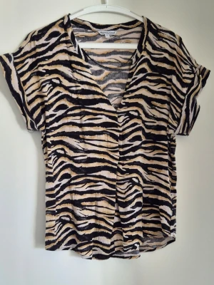 Zebramönstrad blus från Sincerely Love - Cool zebramönstrad blus från Sincerely Love i svart, beige och vitt. Blusen har korta ärmar, v-ringning och ett lätt, luftigt tyg som känns skönt mot huden. 