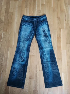 Blå bootcut jeans med leopard mönster  - Säljer ett par blå bootcut jeans från Tornado Mart med unikt leopardliknande mönster längs benen. Jeansen har klassisk femficksdesign, normalhög midja och slitna detaljer för en cool vintagekänsla. 