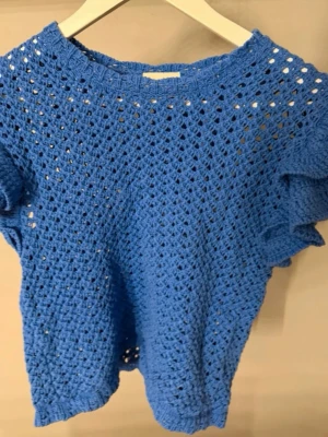 Blå virkad topp från H&M - Snygg blå virkad topp från H&M med korta ärmar och rund hals. Toppen har ett luftigt, hålmönstrat material som ger en avslappnad vibe och passar perfekt till sommaren. Enkel att styla över ett linne eller bikini för en trendig look.
