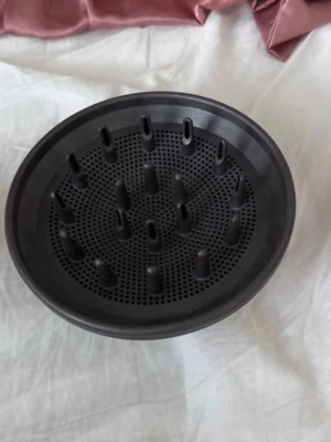 Svart Dyson hårfön-diffuser i plast - En svart rund hårfön-diffuser i tålig plast med flera piggar och små hål för att sprida luftflödet jämnt. Perfekt för att framhäva lockar och ge volym till håret. Passar de flesta standardfönar.