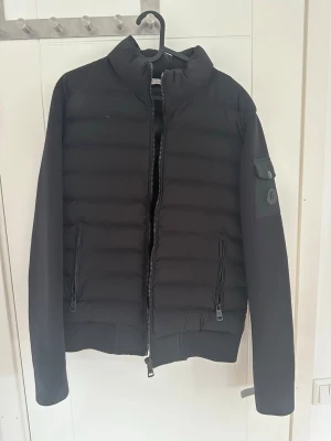 Svart pufferjacka från Moncler svart sällsynt  - Snygg svart pufferjacka från Moncler med quiltad front och släta ärmar. Jackan har hög krage, två dragkedjefickor framtill och en Moncler-logga på ärmen. Perfekt för kalla dagar och har en modern, stilren look.