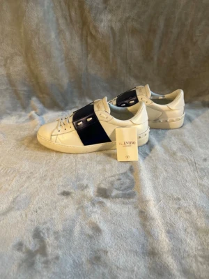 Valentino Garavani vita sneakers - Snygga vita sneakers från Valentino Garavani med en bred mörkblå rem över mitten.😁skorna är bland dem mest populära på marknaden nu.vi checkar igenom produkterna så att de är 100%äkta ✅😁 på köpet ingår ett valentino kort 😁🙌skick 8/10