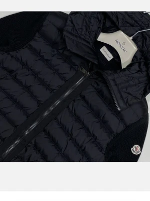 Svart dunjacka från Moncler - Snygg svart dunjacka från Moncler med quiltad design och ribbstickade muddar vid ärmslut och nederkant. Jackan har dragkedja framtill, huva och Moncler-logga på ärmen. Materialet är en mix av dun och stickat tyg som ger både värme och stil.