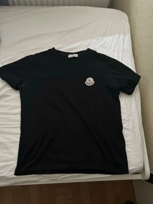 Svart Moncler t-shirt med logga - Snygg svart t-shirt från Moncler med klassisk rund hals och korta ärmar. På bröstet sitter Monclers ikoniska logga som en patch. Perfekt för en clean och stilren look.