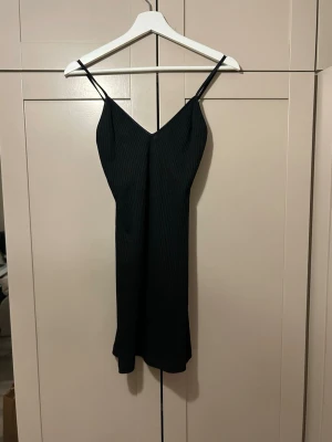 kort ribbad klänning från Chiquelle - Säljer en svart ribbad klänning från Chiquelle med smala axelband och v-ringad hals. Klänningen har en figurnära passform och är i kort modell, perfekt för dig som gillar enkel men stilren design. 