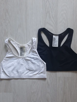 2 sport-bhar från H&M, svart och vit - Två sport-bhar från H&M i svart och vitt. Båda har brottarrygg och meshdetaljer på sidorna och ryggen för extra ventilation. Tillverkade i stretchigt material som ger bra stöd och komfort. Perfekta för träning eller en aktiv vardag.