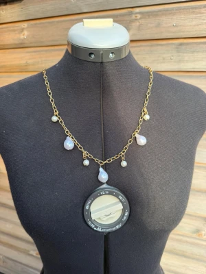 Guldhalsband med droppformade pärlor - Unikt halsband med grov guldfärgad kedja och fem vita droppformade pärlor som hänger längs kedjan. Pärlorna har en skimrande yta och ger halsbandet en elegant och trendig look. Perfekt accessoar för att lyfta vilken outfit som helst.
