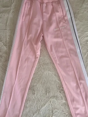 Palm Angels rosa mjukisbyxor - Snygga rosa mjukisbyxor från Palm Angels med vita sidoränder och broderad logga på benet. Byxorna har resår i midjan, raka ben. Stl S herr men passa tjejer också i stl S använda 1 gång inte min stil äkta har kvitto 