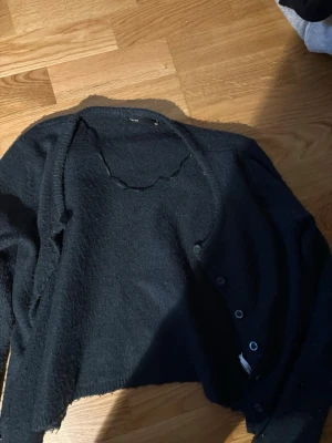Svart kofta med knappar - Mysig svart kofta med knäppning framtill och lång ärm. Koftan har en enkel, rak passform och är tillverkad i ett mjukt, stickat material. Perfekt att slänga över en t-shirt eller topp för en avslappnad look.