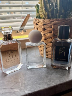 Tre exklusiva parfymer i glasflaskor - Säljer tre snygga parfymer: Kayali Musk 12 i en elegant sexkantig glasflaska med guldton, Lucianne Eau de Parfum i en stilren fyrkantig flaska med vit rund kork, samt Ellis Brooklyn Sci Fi i en mörk glasflaska med svart etikett och silverdetaljer. Reserverade 