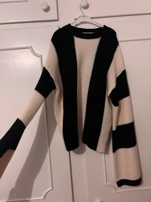 Randig stickad  tröja - Säljer en  stickad tröja med breda svarta och beige ränder. Tröjan har lång ärm och en grovstickad struktur som ger en cool och avslappnad look. Ganska tajt i midjan liksom inte ”lös” 