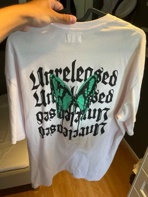 Vit t-shirt med fjäril från Yourturn - Vit t-shirt från Yourturn med svart text 'Unreleased' på bröstet och stor grön fjäril med text på ryggen. Oversized passform och tillverkad i mjuk bomull. 
