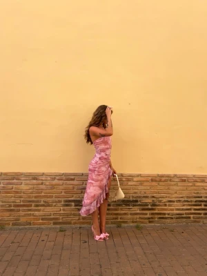 Rosa omlottklänning med volang - Säljer en snygg rosa omlottklänning med volangkant och asymmetrisk nederdel. Klänningen är axelbandslös och har ett mönster i olika rosa nyanser. Perfekt för sommarens alla tillfällen! Priset som syns är vad som gäller🩷🎀✨☀️