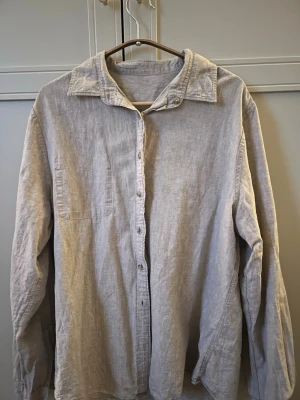 Beige linneskjorta med knappar - Luftig och stilren beige skjorta i linne med klassisk krage och knäppning framtill. Skjortan har långa ärmar och en bröstficka, perfekt för en avslappnad men snygg look. Passar till både jeans och kjol.