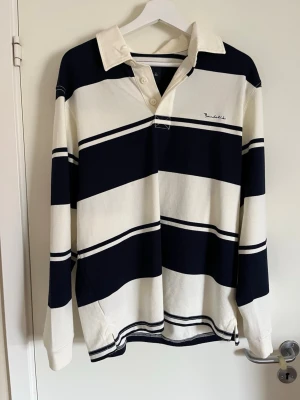 Old school tröja från Bondelid - Säljer en klassisk långärmad rugbytröja från Bondelid ALDRIG ANVÄND, med breda marinblå och vita ränder. Skjortan har krage, knappar i halsen och en relaxed passform. Perfekt för dig som gillar sportig och avslappnad stil. 