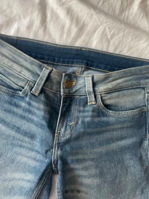 Ljusblå bootcut jeans med slitningar - Säljer ett par ljusblå bootcut jeans med snygga slitningar och klassisk femficksdesign knappast använda. Jeansen har normalhög midja och är tillverkade i denim med lätt stretch. Perfekta för en avslappnad och trendig look.