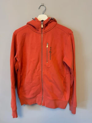 Sail racing hoddie - Snygg hoodie från Sail Racing med dragkedja framtill och en praktisk bröstficka med zip. Hoodien har justerbar huva med snören och mjukt fleecefoder på insidan. Perfekt för dig som gillar sportig och avslappnad stil. Självklart äkta✅