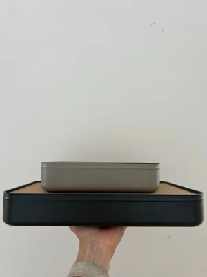 Två förvaringslådor i metall  - Säljer två förvaringslådor i metall. Den undre stora är svart och den lilla är grå-beige med praktiska fack för sortering. Perfekt för att organisera småprylar, smink eller kontorssaker. Modern och enkel design som passar i de flesta rum.