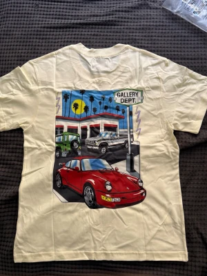 Gul t-shirt från Gallery Dept. - Cool gul t-shirt från Gallery Dept. med tryck av bilar och palmer på ryggen samt logga framtill. T-shirten har rund hals och korta ärmar. Perfekt för dig som gillar streetwear och unika motiv.