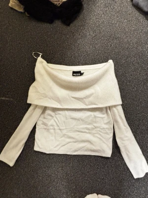 Vit off shoulder stickad tröja - Säljer en vit stickad off shoulder-tröja från Pieces. Tröjan har långa ärmar och en bred, vikt krage som ger en snygg och trendig look. Perfekt att styla med jeans eller kjol för en cool outfit.