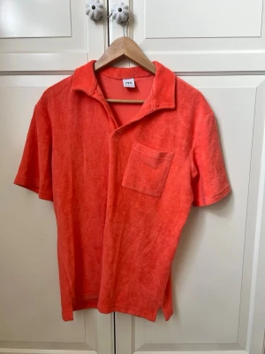 Orange frottéskjorta från Zara - Säljer en orange coral skjorta från Zara i mjuk frotté. Skjortan har korta ärmar, öppen krage och en bröstficka. Perfekt för dig som gillar en avslappnad och trendig stil. Enkel att matcha med jeans eller shorts.