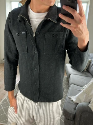 Stickad Cardigan/Overshirt - Säljer nu denna väldigt snygga och trendiga cardigan/overshirt! Mörk grå. Mått: A:48 B:48 C:50 D:63 (cm) Skriv vid fundering 😇🙌
