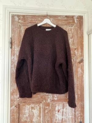Brun fluffig stickad tröja - Mysig brun stickad tröja med rund hals och lång ärm. Tröjan har en fluffig, lite luddig yta och en avslappnad passform. Tillverkad i Alpacka ull.