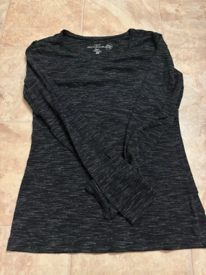 Svart långärmad topp från H&M - En svart långärmad topp från H&M med diskret melerat mönster. Toppen har rund halsringning och är tillverkad i mjuk bomullsblandning. Perfekt att styla med jeans eller kjol för en enkel och snygg look.