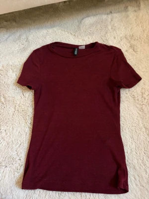 Vinröd basic t-shirt från H&M - En enkel vinröd t-shirt från H&M i mjuk bomull. Modellen är klassisk med rund halsringning och korta ärmar. Perfekt att matcha med jeans eller kjol för en clean look. Se bild 2 för genomskinlighet
