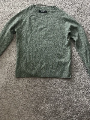 Grön stickad tröja från Vero Moda - Mysig grönmelerad stickad tröja från Vero Moda. Tröjan har rund halsringning, långa ärmar och ribbade muddar vid ärmslut och nederkant. Perfekt för lager på lager och enkel att matcha med jeans eller kjol. 