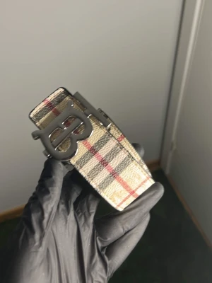Bälte + plånbok - Snyggt bälte med klassiskt rutmönster i beige, svart och rött. Bältet har ett stort metallspänne med BB-logga och är tillverkat i skinn. Perfekt accessoar för att lyfta din outfit.