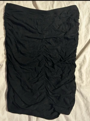 Svart kjol  - Säljer en svart kortkjol med rynkade detaljer framtill. Enkel, stilren design som funkar till nästan allt i garderoben. Mjukt och stretchigt material för en bekväm passform. En riktig bas-kjol som alltid funkar(ifrån shein).