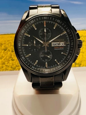 Svart Champion Spider Sport klocka - Stilren svart klocka från Champion Spider Sport med metallarmband och rund urtavla. Klockan har kronograf, datumvisning och tydliga indexmarkeringar. Perfekt accessoar för dig som gillar sportig men ändå klassisk stil.Nyligen servad med nytt batteri, säljes i befintligt skick enligt bilderna!