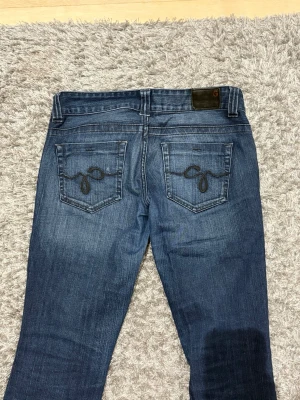 Blå bootcut jeans med broderade fickor - Snygga blå bootcut jeans med broderade detaljer på bakfickorna. Jeansen har en klassisk femficksmodell och en mörk tvätt med lätt slitning. Perfekta för dig som gillar en avslappnad men ändå trendig look.