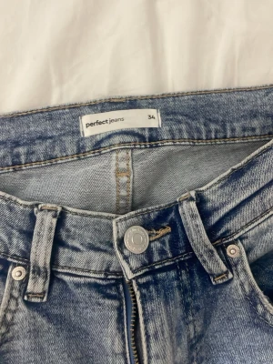 Ljusblå bootcut jeans från Perfect Jeans - Säljer ett par ljusblå bootcut jeans från Perfect Jeans. Jeansen har klassisk femficksdesign, hög midja och dragkedja med knapp. Materialet är denim i bomull och passformen är utsvängd nedtill för en trendig look.